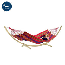 Load image into Gallery viewer, A colourful Aruba Cayenne hammock with a wooden stand, featuring a person lying on it, set against a white background.