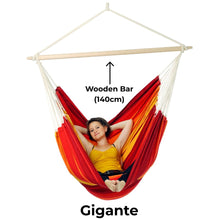 Load image into Gallery viewer, Red and yellow hammock with wooden bar labelled, featuring a person relaxing.
