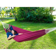 Load image into Gallery viewer, Two people in a red hammock on a grassy area with trees in the background
