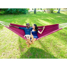Load image into Gallery viewer, Two people relaxing in a pink hammock on a grassy field.

